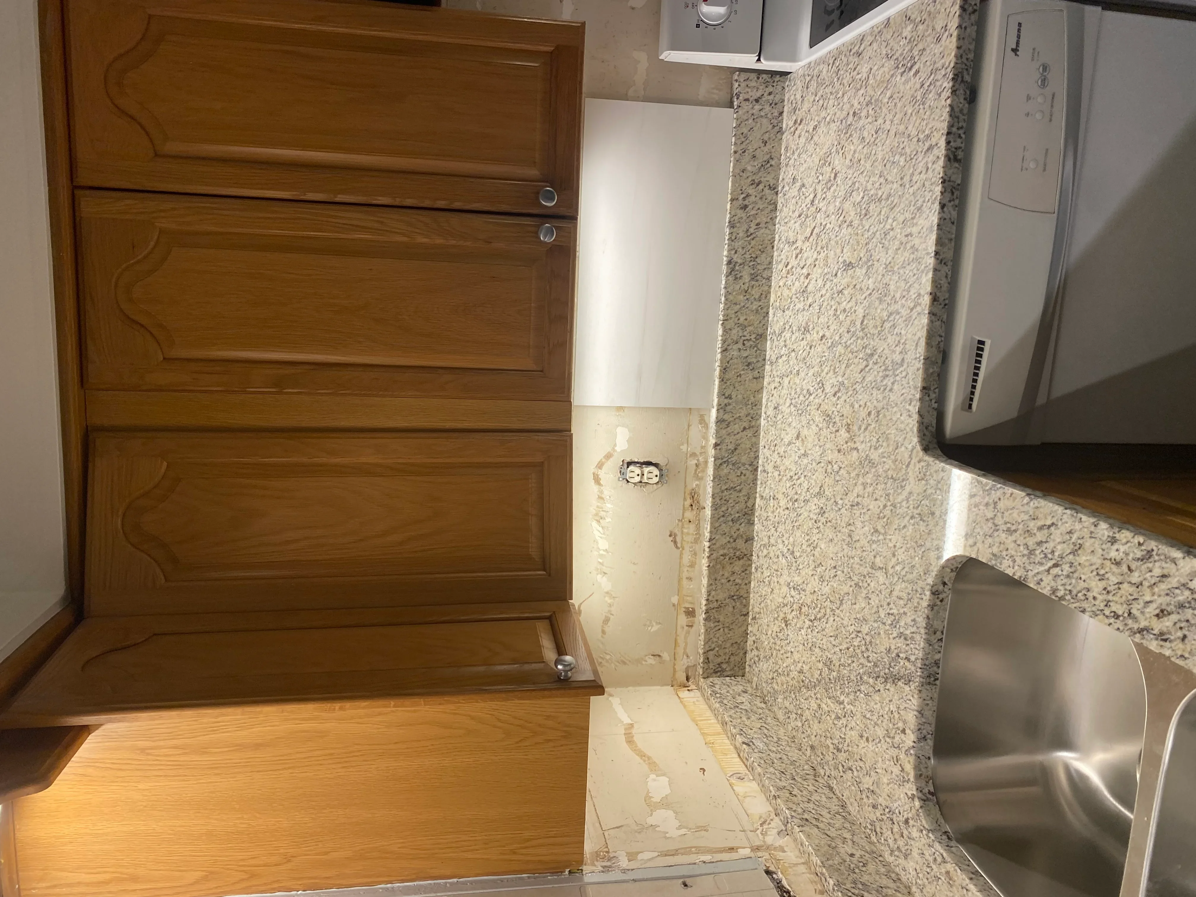 New electrical outlet installed in kitchen wall with granite countertop and wooden cabinets