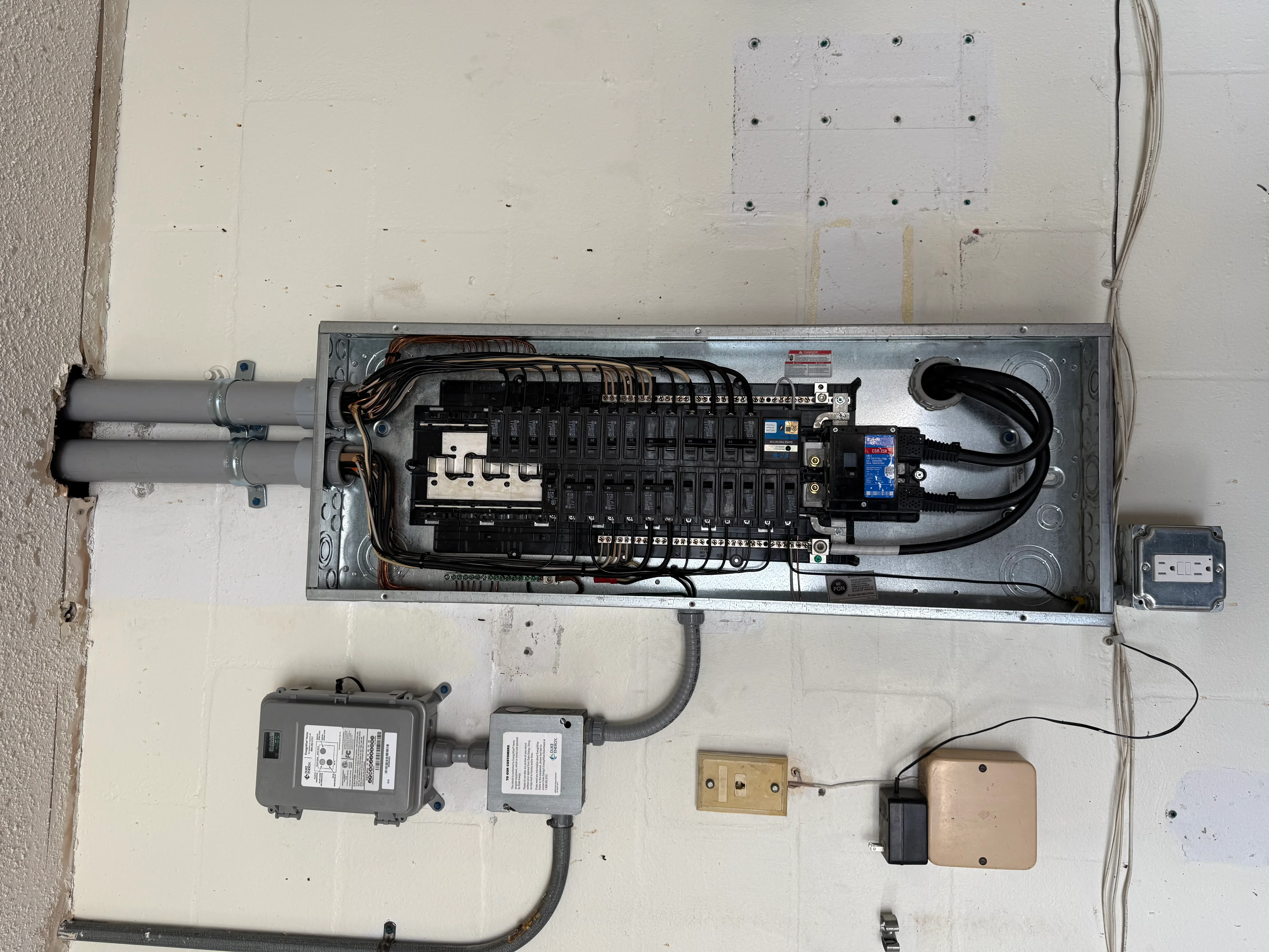 Electrical panel with breaker box, organized circuits, conduit, and disconnect boxes installed on drywall